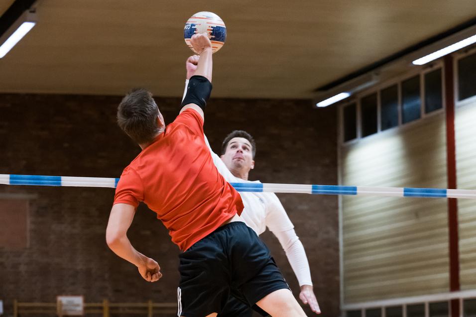 Zwei Spieler im Sprung während eines Handballspiels, einer wirft den Ball über eine Markierung.